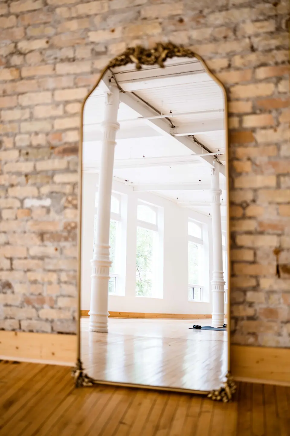 Ornate antique floor mirror leaning on the exposed brick wall