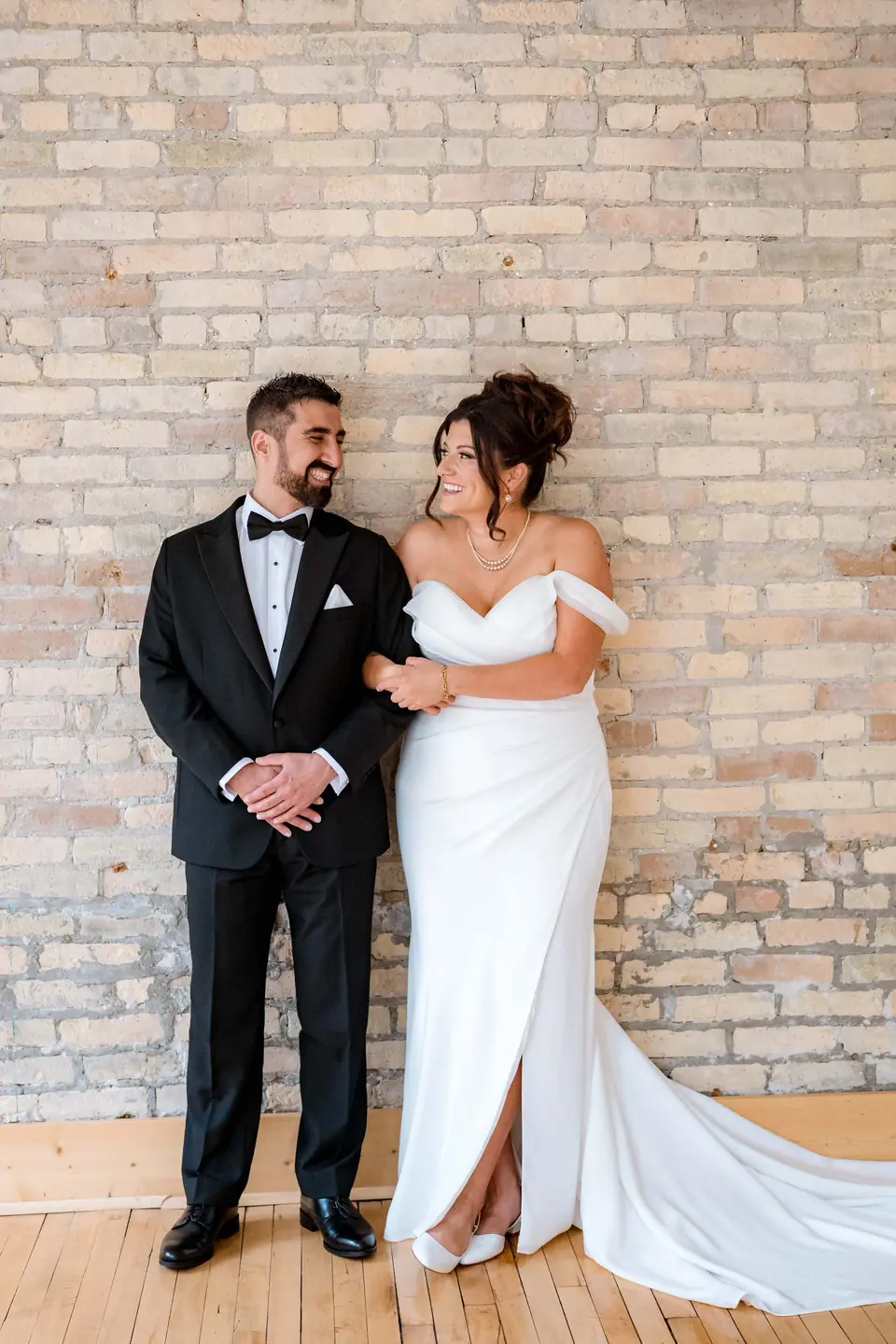 Bride and groom laughing together against the exposed brick wall