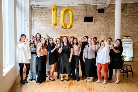 Team of colleagues celebrating with gold number balloons against the brick wall