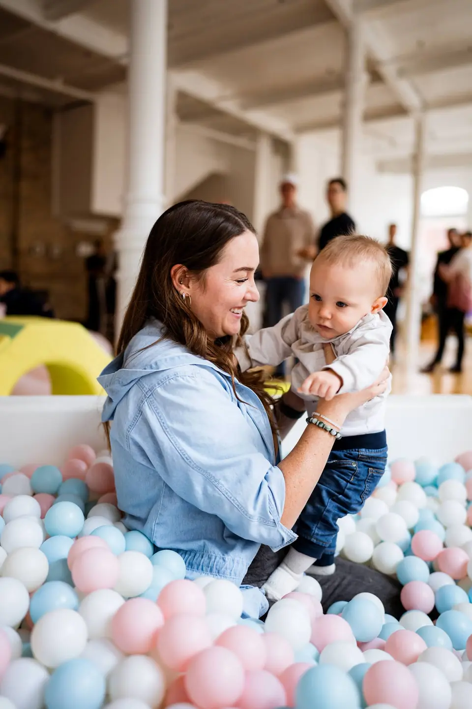 Mother and baby laughing together in a pastel ball pit