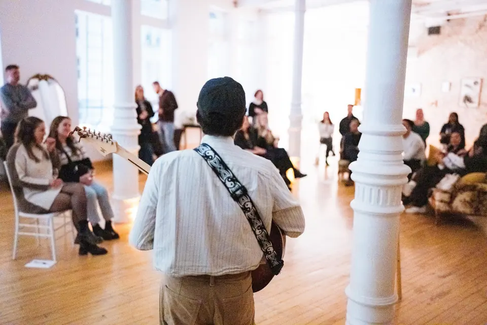 Guitarist performing to an audience seated among the white columns