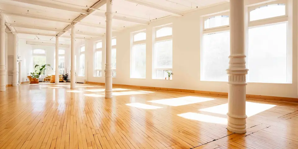 Sunlit main hall of The Harlow Exchange with white columns, tall windows and hardwood floors
