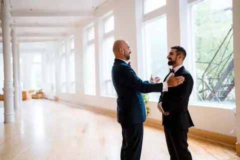 Two grooms sharing a first look by the windows in the main hall